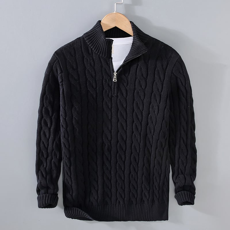 Schwarzer Strickpullover mit Zopfmuster und Reißverschluss, hängend an einem Holzkleiderbügel vor grauem Hintergrund. Wintermode, Herrenbekleidung.