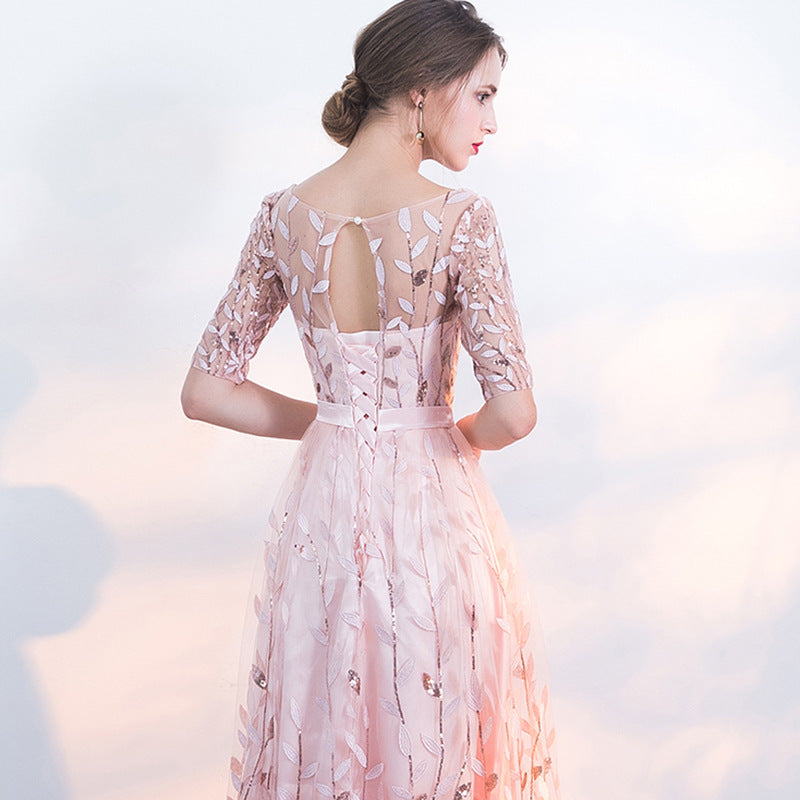 Frau in elegantem, rosa Abendkleid mit floralen Spitzenmustern und halblangen Ärmeln, Rückenausschnitt, stilvoller Look, festliche Mode.