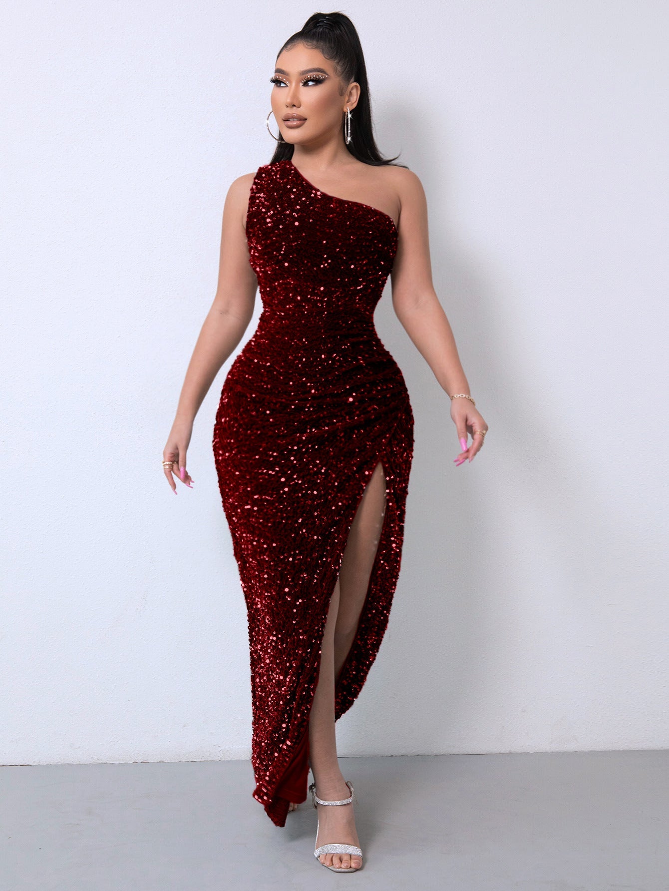 Frau in elegantem, rotem Paillettenkleid mit hohem Schlitz, posiert vor weißer Wand. Abendmode, glamouröses Design, festliche Kleidung.