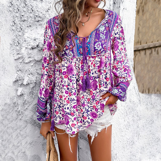 Frau in lila geblümter Boho-Bluse und weißen Shorts vor weißer Wand. Sommermode, Boho-Stil, lässiges Outfit, trendige Damenbekleidung.