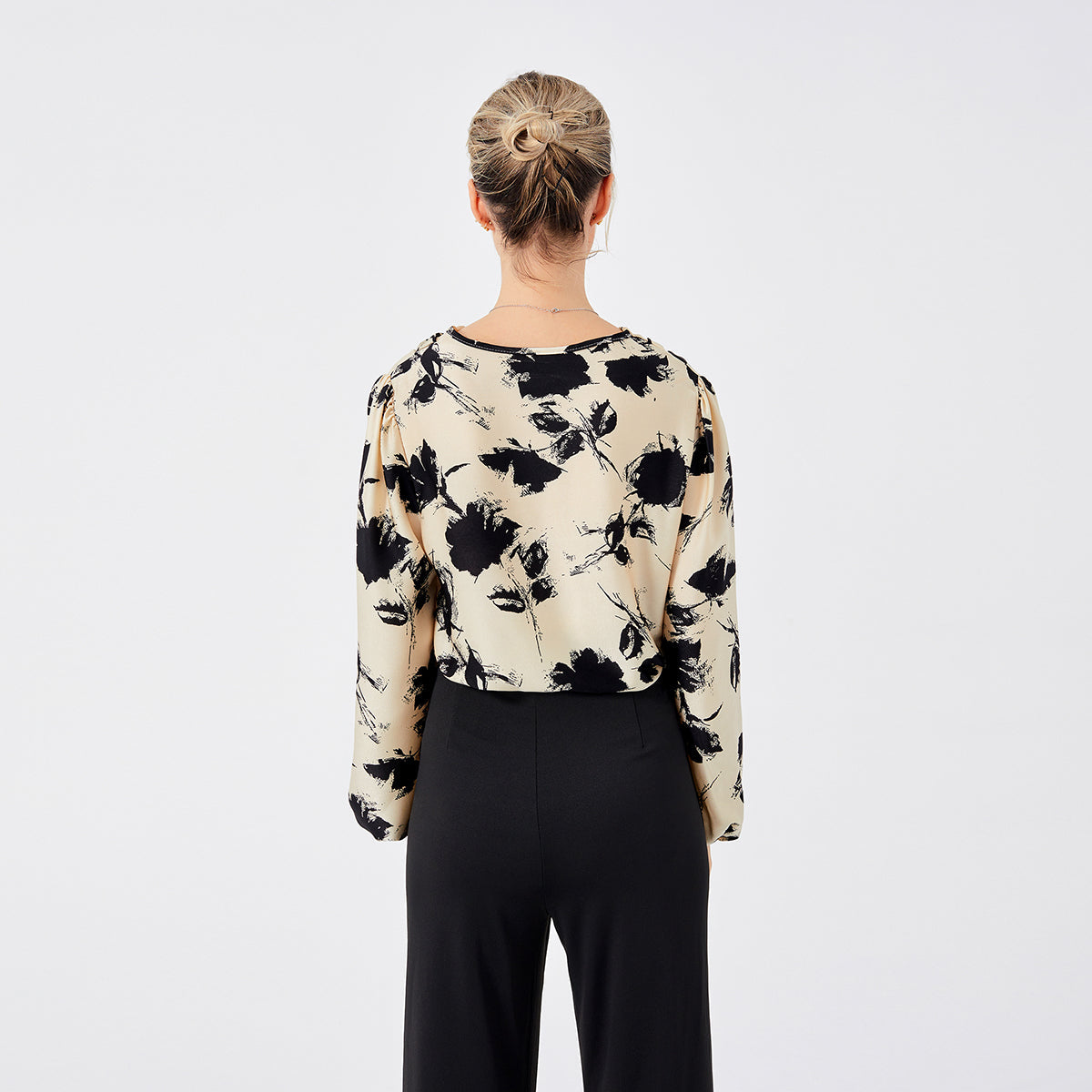 Frau in eleganter Bluse mit schwarzem Blumenmuster, Rückansicht. Modetrend, Damenbekleidung, stilvolle Oberteile, Herbstmode 2023.