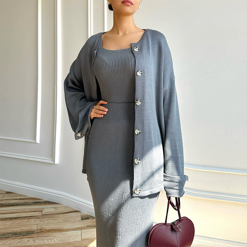 Elegante Frau in grauem Strickkleid und passender Strickjacke, hält eine herzförmige rote Handtasche. Mode, Damenbekleidung, Herbsttrends.