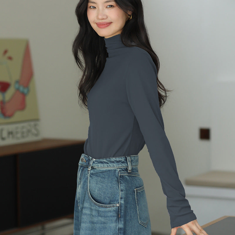 Frau in dunkelgrauem Rollkragenpullover und blauer Jeans, lächelnd in modernem Raum. Mode, Damenbekleidung, lässiger Stil.
