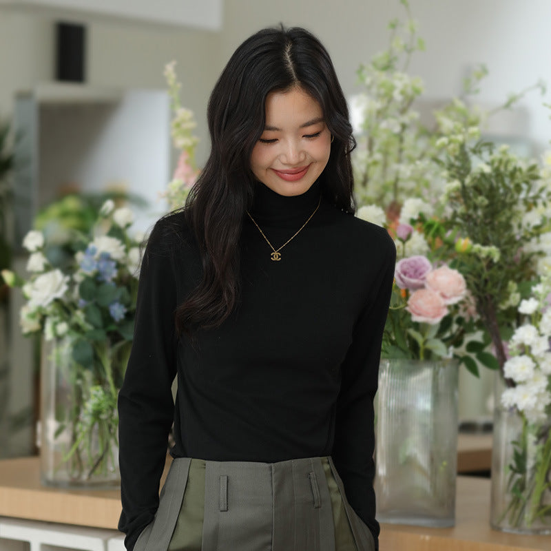 Frau in schwarzem Pullover vor Blumenarrangement, lächelnd. Elegante Mode, asiatische Frau, Blumenhintergrund, stilvolles Outfit, Innenraum.
