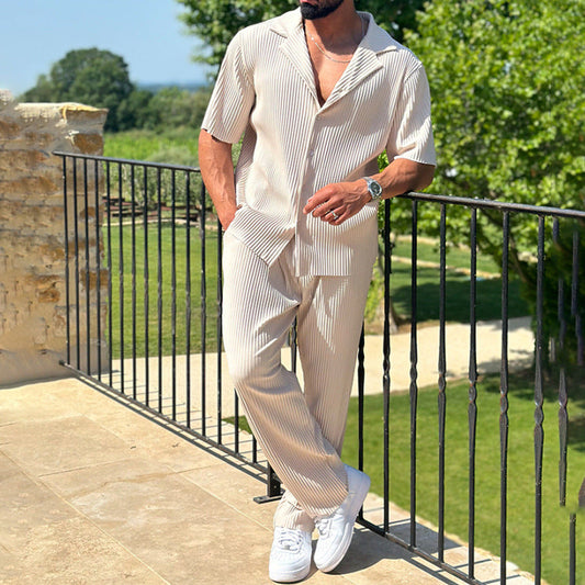 Mann in gestreiftem Sommeranzug auf Balkon, trägt weiße Sneaker und Armbanduhr, umgeben von Natur. Elegante Herrenmode, Freizeitlook.