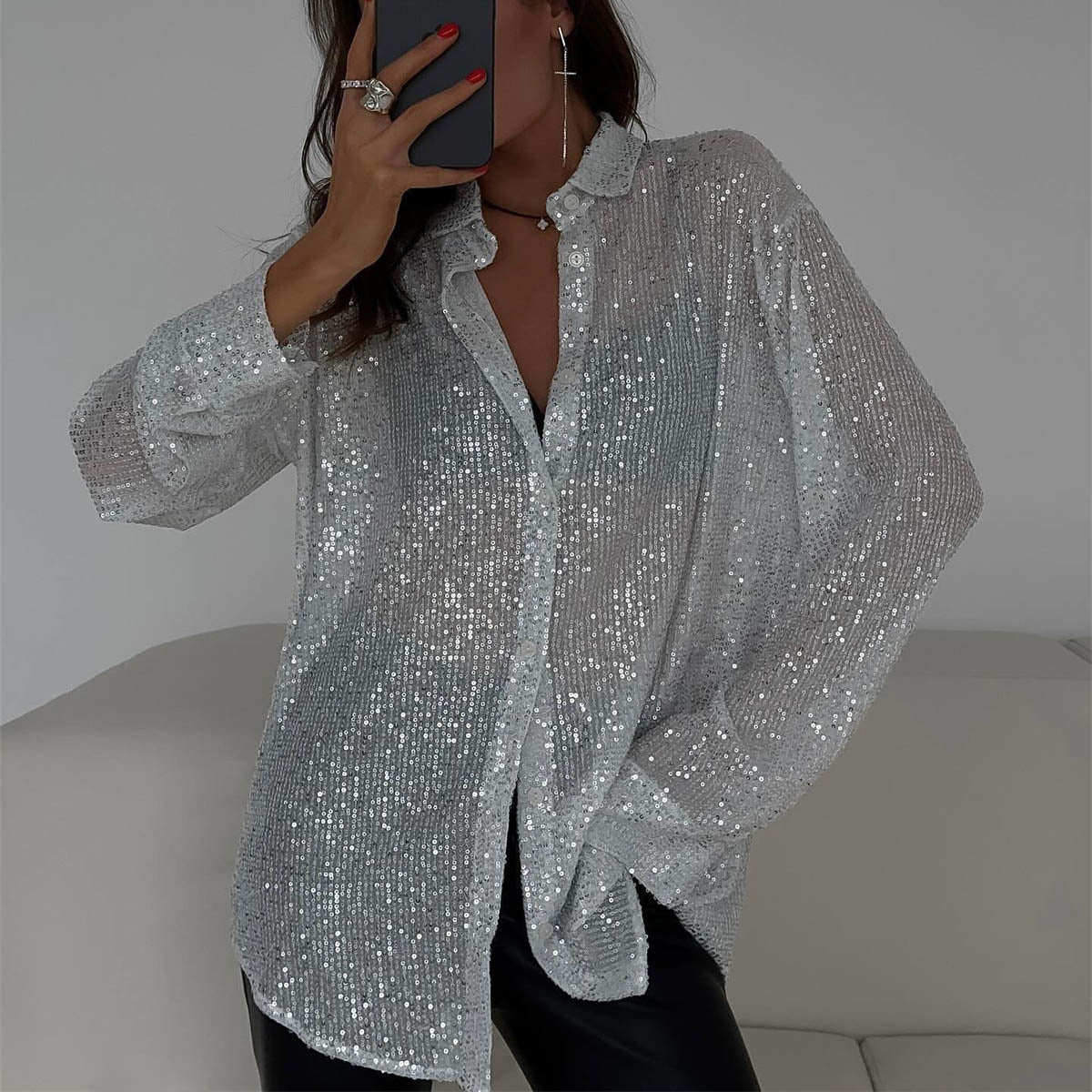 Frau in silberner Paillettenbluse, posiert auf weißem Sofa. Glitzerndes Hemd, modisches Outfit, eleganter Look, trendige Damenmode.