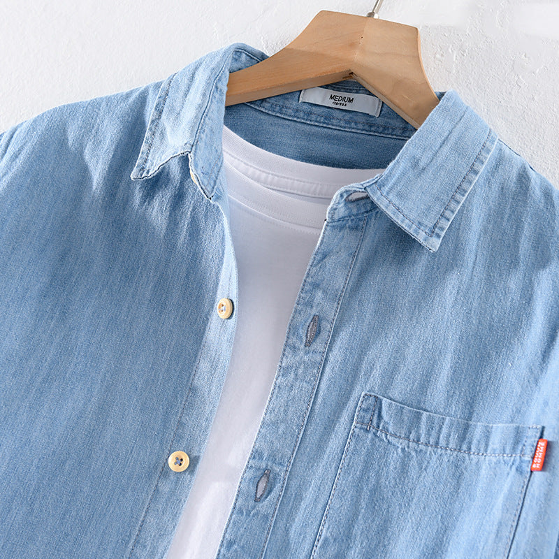Hellblaues Jeanshemd auf Holzkleiderbügel, über weißem T-Shirt. Modetrend, lässiger Stil, Denim-Oberbekleidung, Herrenmode, Freizeitlook.