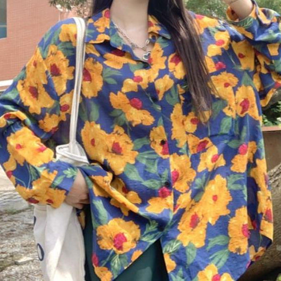 Frau trägt bunte Bluse mit gelbem Blumenmuster, hält weiße Stofftasche. Modetrend, florales Design, lässiger Stil, Herbstmode.