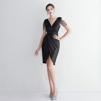 Frau in elegantem, schwarzem Paillettenkleid mit V-Ausschnitt und verzierten Ärmeln, posiert vor weißem Hintergrund. Abendmode, glamouröses Design.
