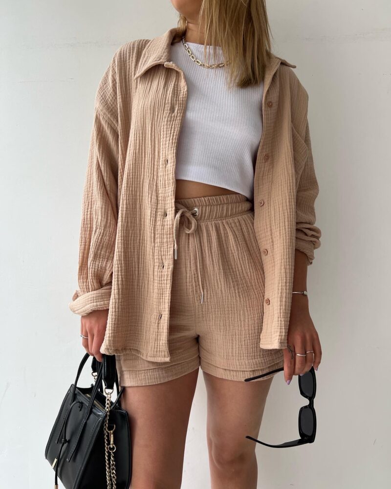 Frau in beigem Freizeit-Set aus Hemd und Shorts, weißes Top, schwarze Tasche und Sonnenbrille. Modetrend, lässiger Sommerlook, Damenbekleidung.
