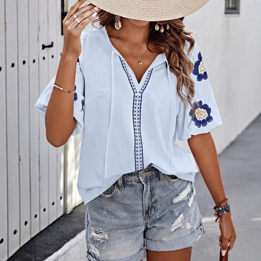 Frau in blauer bestickter Bluse und zerrissenen Jeansshorts, trägt Strohhut, steht vor weißer Wand. Sommermode, lässiger Stil, Boho-Chic.