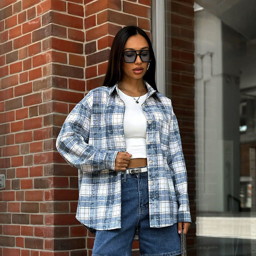 Frau in kariertem Hemd und Jeansrock vor Backsteinwand, trägt Sonnenbrille und weißes Top. Streetstyle Mode, urbaner Look, trendige Kleidung.