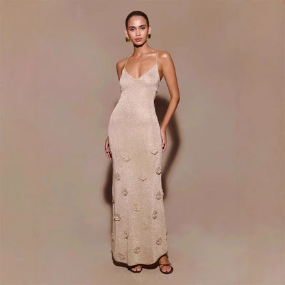Eine Frau trägt ein elegantes, langes, beige Abendkleid mit Spaghettiträgern und Blumenmuster, posierend vor neutralem Hintergrund.