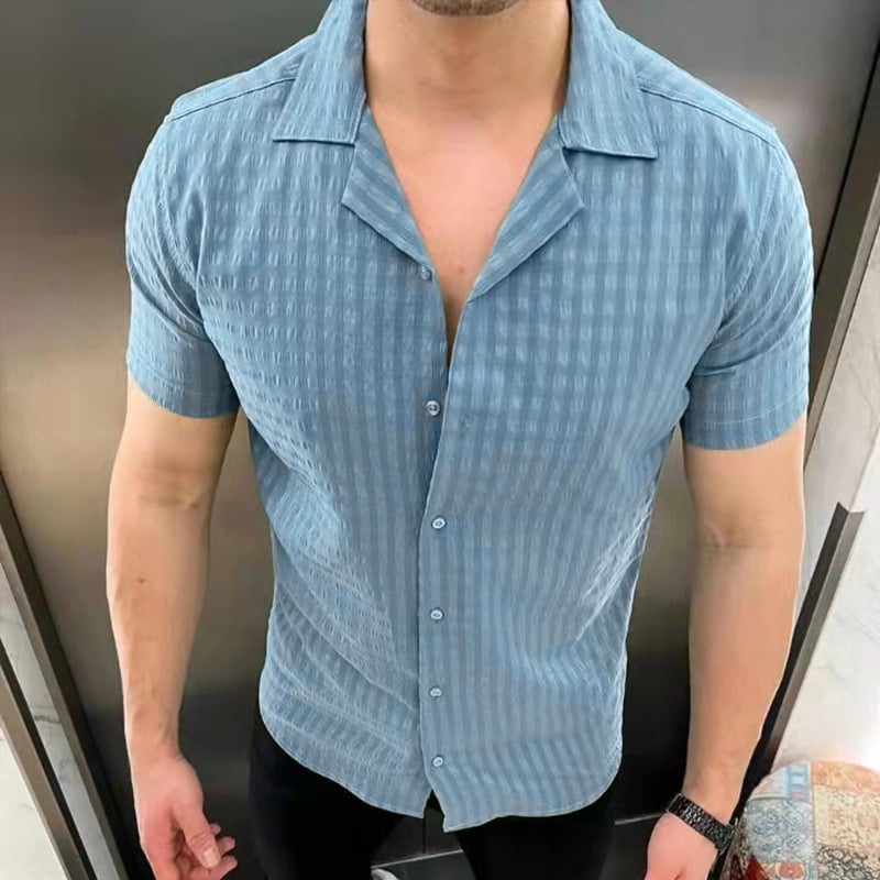Mann in hellblauem, kurzärmligem Hemd mit Knopfleiste, stehend vor einem grauen Hintergrund. Modetrend, Herrenbekleidung, Sommerlook.