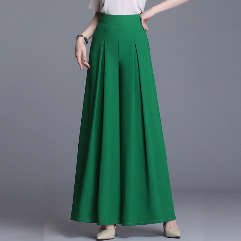 Frau in grüner, weiter Palazzo-Hose und weißem Oberteil, posiert vor grauem Hintergrund. Modetrend, elegante Damenbekleidung, stilvolle Hose.