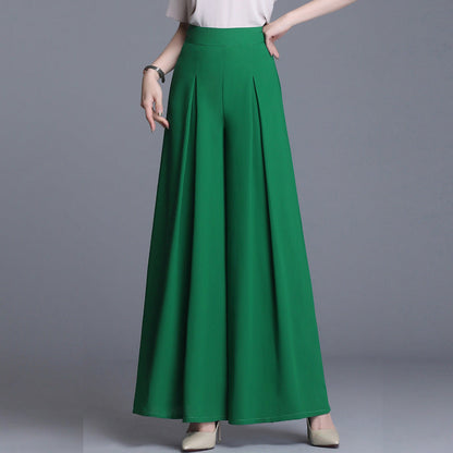 Frau in grüner, weiter Palazzo-Hose und weißem Oberteil, posiert vor grauem Hintergrund. Modetrend, elegante Damenbekleidung, stilvolle Hose.