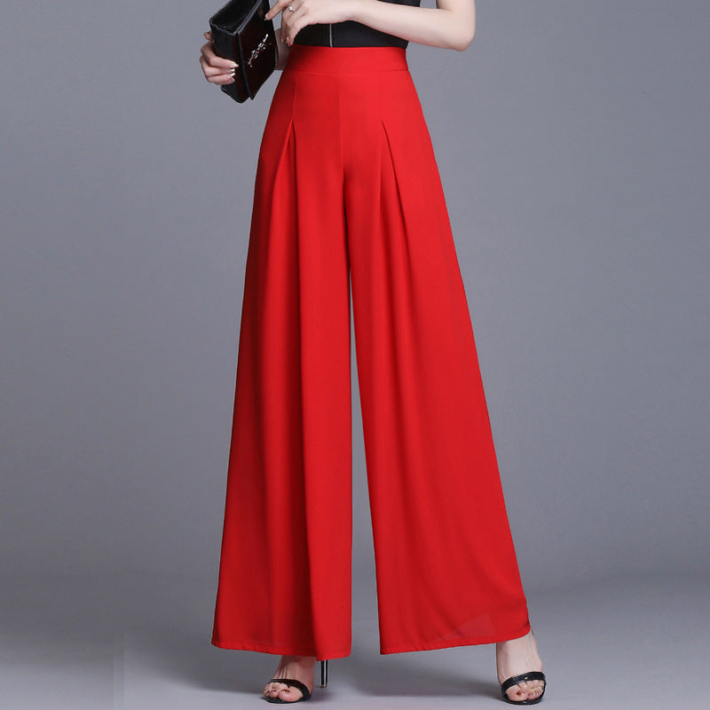 Frau in eleganter roter Palazzo-Hose, schwarze High Heels, grauer Hintergrund. Modetrend, Damenbekleidung, stilvolle Hosenmode.