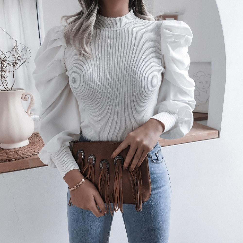 Frau in weißem Pullover mit Puffärmeln, blaue Jeans, hält braune Fransenhandtasche. Modetrend, eleganter Look, stilvolle Damenmode.