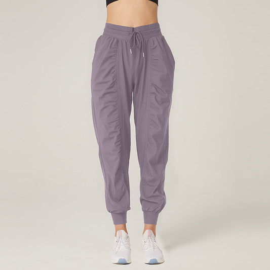 Frau in lila Jogginghose und weißen Sneakers vor neutralem Hintergrund. Bequeme Sportbekleidung, modische Damenhose, Freizeitlook.