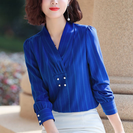 Frau in eleganter blauer Bluse mit Perlenknöpfen, stehend vor Säule. Modetrend, Damenmode, stilvolle Kleidung, Büro-Outfit.