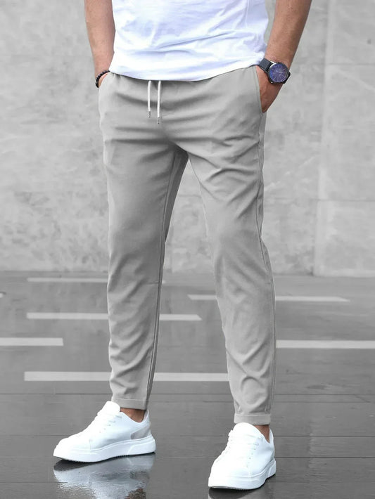 Mann in grauer Jogginghose und weißen Sneakers vor grauem Hintergrund. Lässige Herrenmode, sportlicher Look, moderne Freizeitkleidung.