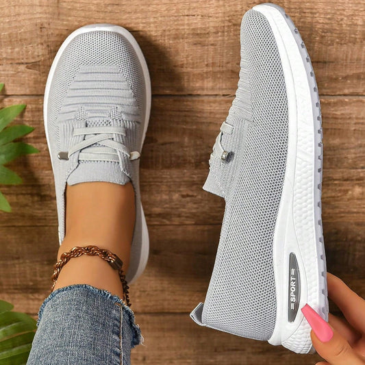 Graue Damen-Sneaker mit Strickmuster, weißer Sohle und Schnürsenkeln auf Holzuntergrund. Modische Freizeitschuhe, ideal für Alltag und Sport.