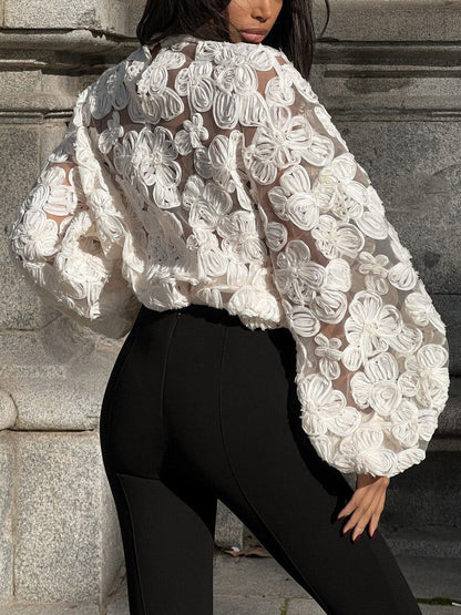 Frau in weißer, transparenter Bluse mit Blumenmuster und schwarzen Leggings vor steinernem Hintergrund. Modetrend, stilvolle Damenbekleidung.