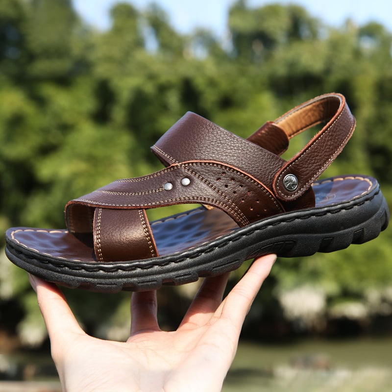 Braune Ledersandale mit robustem Profil, handgehalten vor unscharfem Naturhintergrund. Bequeme Herrensandale, ideal für Sommer und Outdoor.