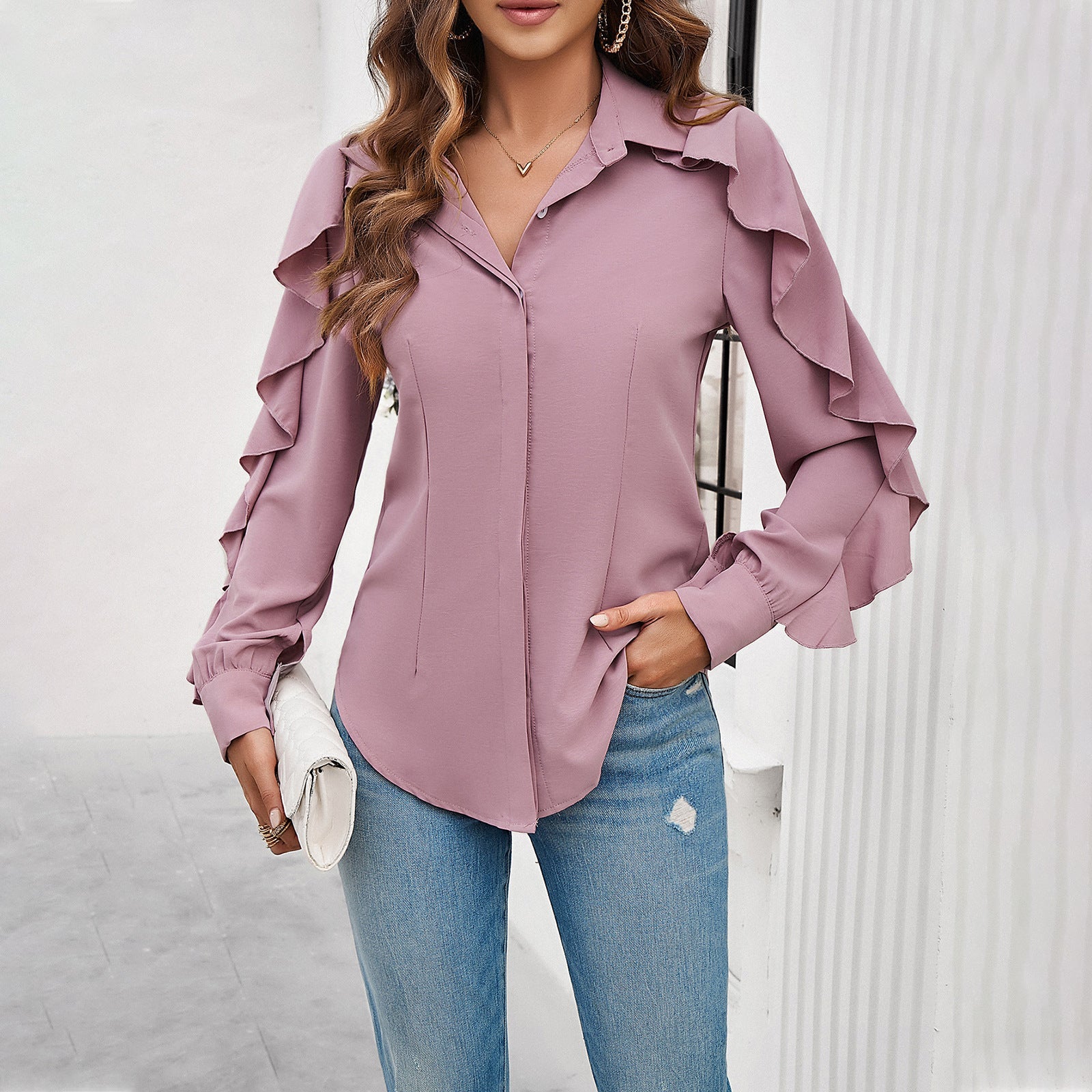 Frau in rosa Rüschenbluse und blauen Jeans, hält weiße Clutch. Modetrend, elegante Damenbekleidung, stilvolles Outfit für Freizeit und Büro.