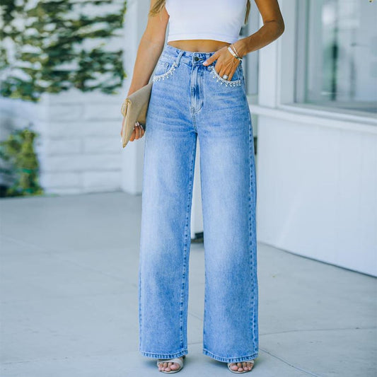 Frau in blauer High-Waist-Jeans und weißem Crop-Top, hält eine beige Clutch. Modetrend, lässiger Sommerlook, Damenmode, Streetstyle.