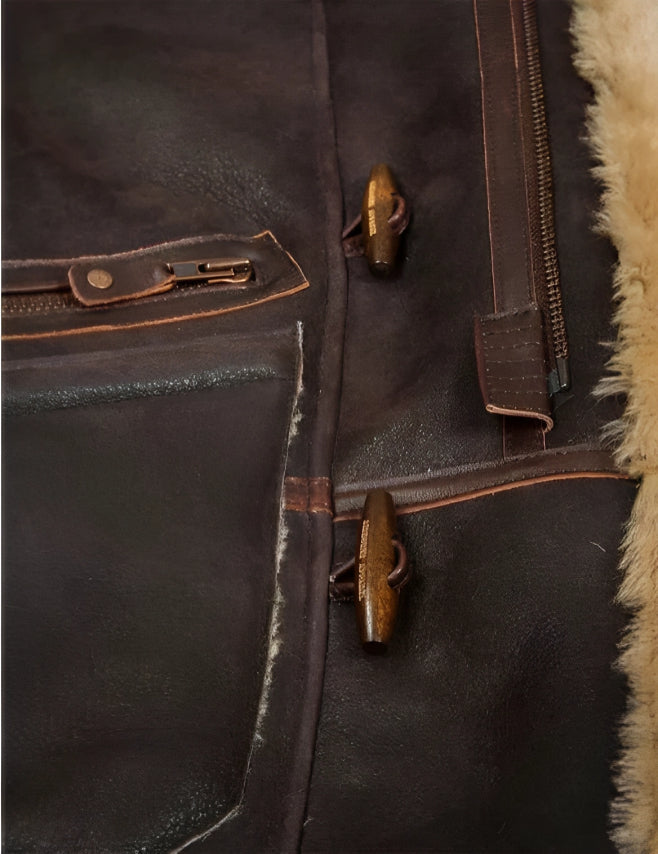 Nahaufnahme einer braunen Lederjacke mit Reißverschluss und Knebelknöpfen, gefüttert mit beigem Lammfell. Hochwertige Wintermode, stilvoll und warm.
