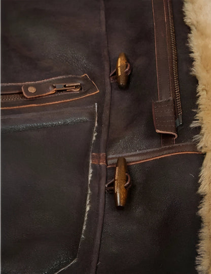 Nahaufnahme einer braunen Lederjacke mit Reißverschluss und Knebelknöpfen, gefüttert mit beigem Lammfell. Hochwertige Wintermode, stilvoll und warm.