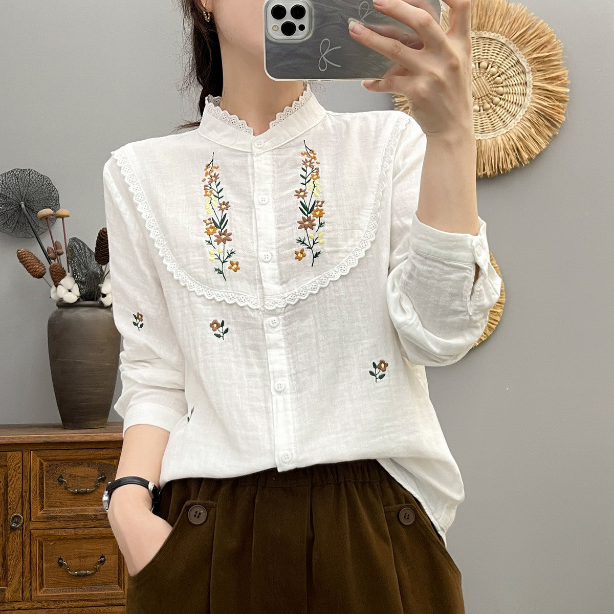 Frau in weißer, bestickter Bluse mit Blumenmuster, fotografiert vor einem Spiegel. Modetrend, Damenmode, Stickerei, eleganter Look.