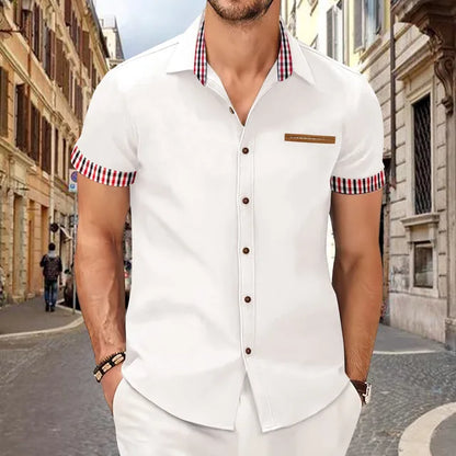 Mann in weißem Kurzarmhemd mit karierten Details, steht auf einer gepflasterten Straße in einer europäischen Stadt. Elegante Herrenmode, Sommeroutfit.