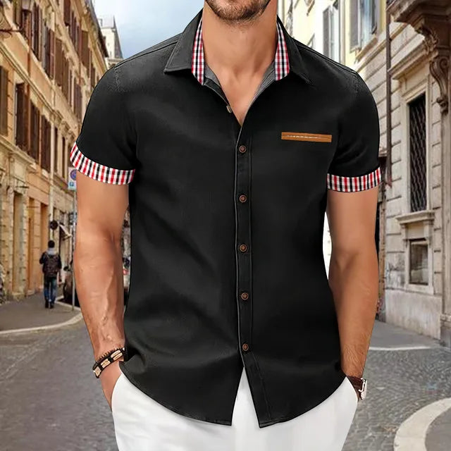 Mann in schwarzem Hemd mit karierten Details, steht auf einer gepflasterten Straße in einer europäischen Stadt. Mode, Herrenbekleidung, urbaner Stil.