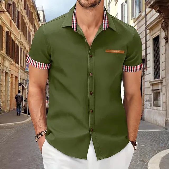 Mann in olivgrünem Kurzarmhemd mit karierten Details, steht auf einer gepflasterten Straße in einer europäischen Stadt. Mode, Herrenbekleidung, Sommerlook.