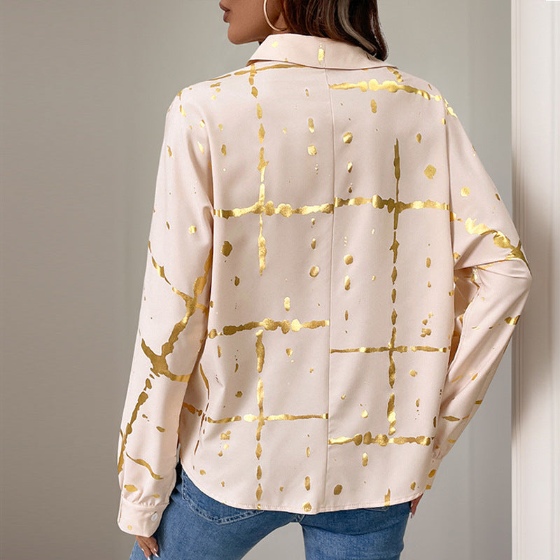Frau trägt cremefarbene Bluse mit goldenen geometrischen Mustern, kombiniert mit blauen Jeans. Elegante Damenmode, stilvolles Design.
