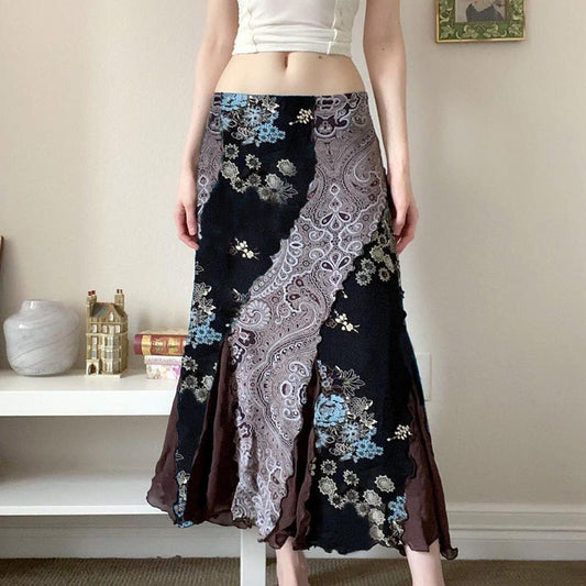 Frau trägt langen, gemusterten Rock mit floralen und Paisley-Motiven. Elegante Mode, Boho-Stil, Wohnzimmer-Hintergrund, trendige Damenbekleidung.