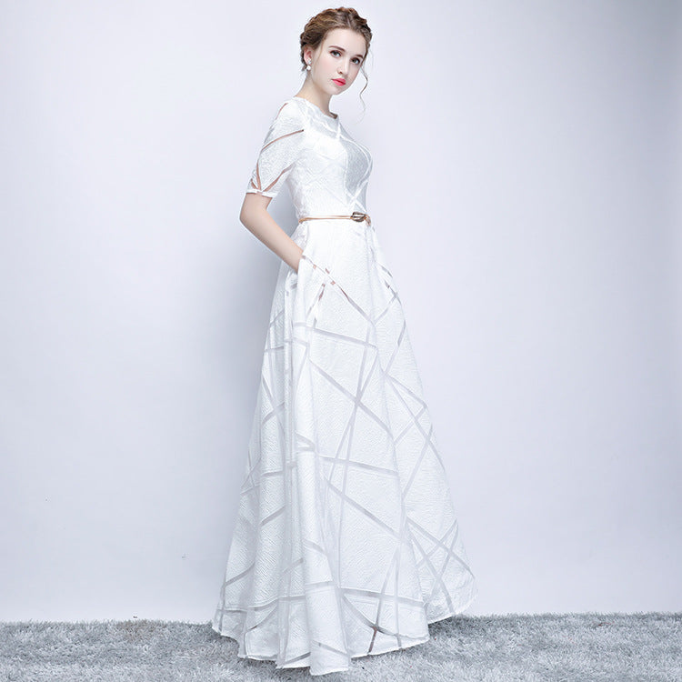 Elegantes weißes Abendkleid mit geometrischem Muster, kurzen Ärmeln und Gürtel, getragen von einer Frau auf grauem Teppichboden.