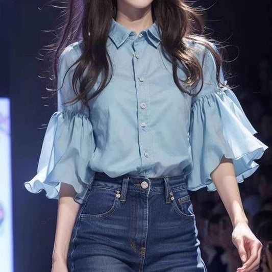 Frau in blauer Bluse mit Rüschenärmeln und hoch taillierter Jeans auf Laufsteg. Modetrend, Damenmode, eleganter Look.