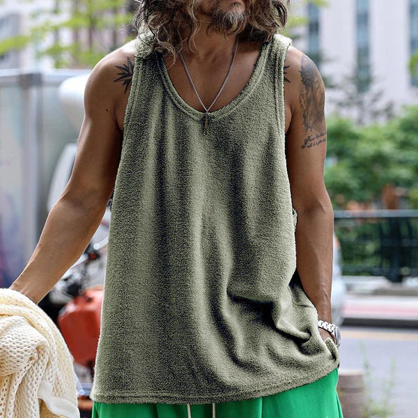 Mann in grünem Tanktop und grüner Hose, trägt Halskette, steht draußen in urbaner Umgebung. Sommermode, lässiger Stil, Herrenbekleidung.