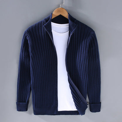 Dunkelblauer Strick-Cardigan mit Reißverschluss, über weißem T-Shirt, auf Holzbügel vor grauer Wand. Modische Herrenbekleidung, Herbstmode.