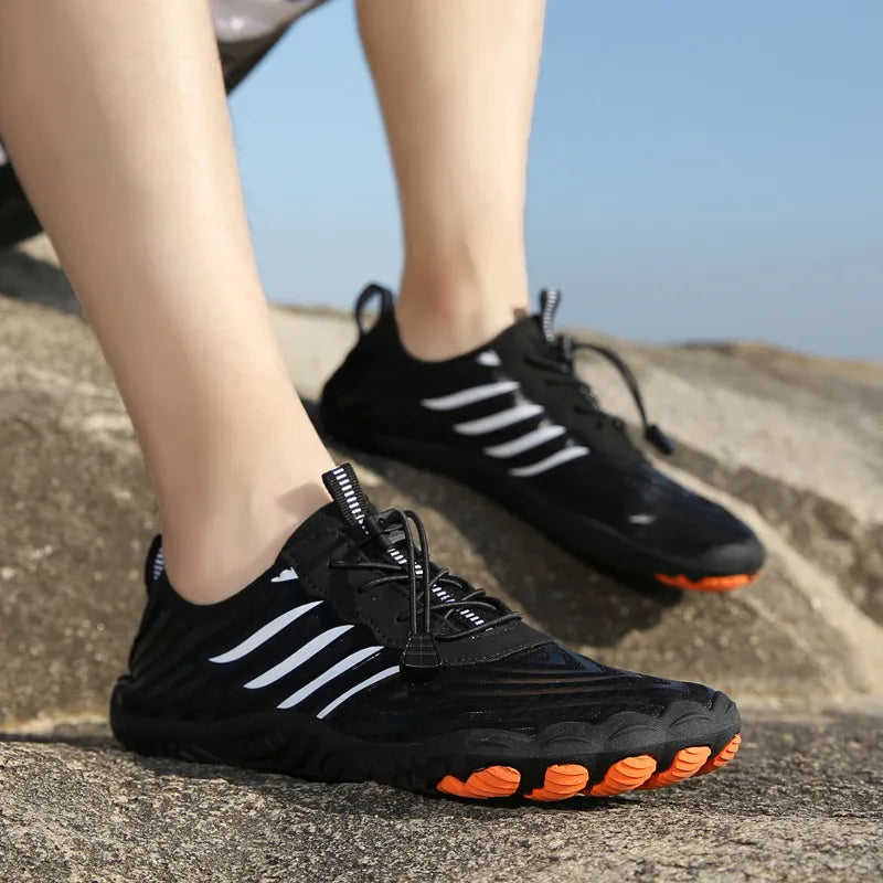 Schwarze Outdoor-Sportschuhe mit weißen Streifen und orangefarbenen Sohlen auf Felsen. Ideal für Wandern und Trekking. Bequeme, rutschfeste Sneakers.
