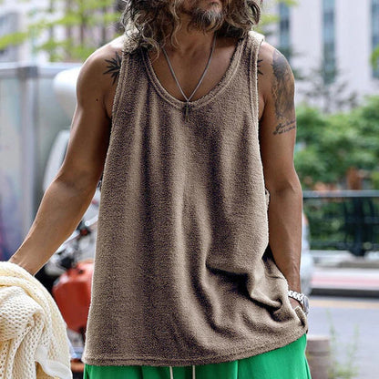 Mann in braunem Tanktop und grüner Hose auf Straße, trägt Halskette. Urbaner Stil, Sommermode, lässiges Outfit.