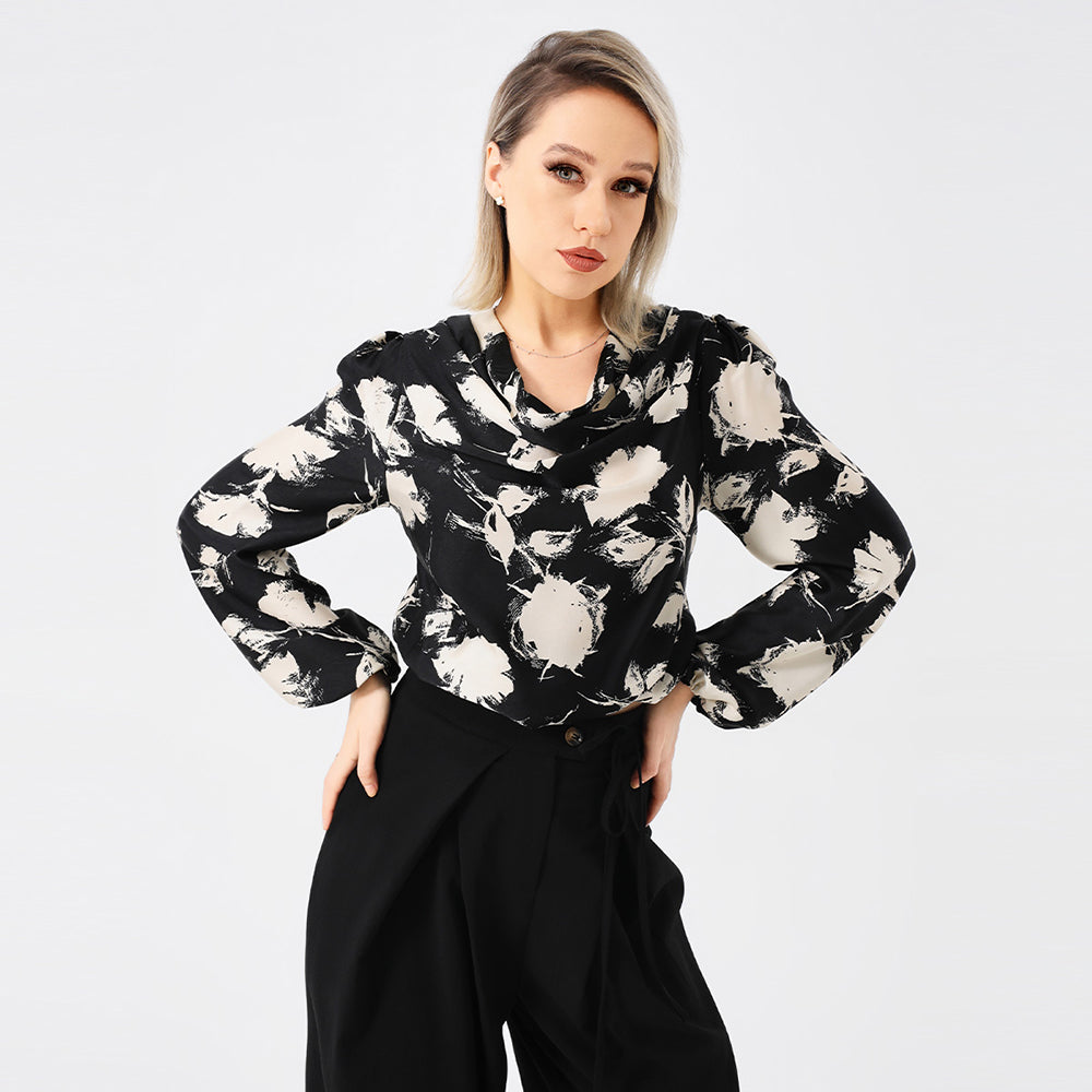 Frau in stilvoller schwarz-weißer Bluse mit abstraktem Muster, posiert vor weißem Hintergrund. Modetrend, Damenbekleidung, eleganter Look.