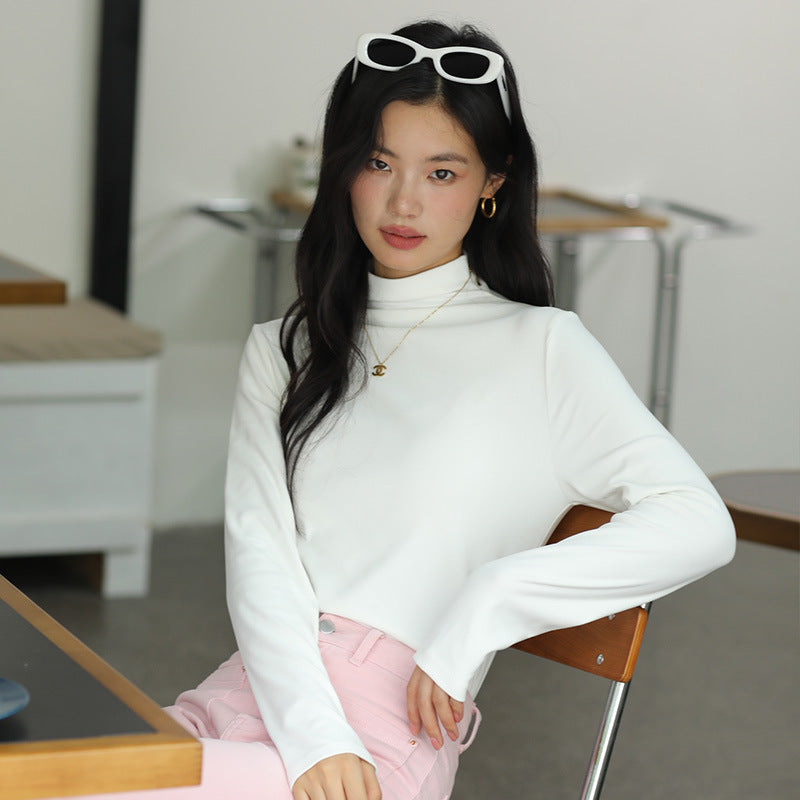 Junge Frau mit weißem Rollkragenpullover und Sonnenbrille im Haar sitzt auf einem Stuhl. Elegante Mode, lässiger Stil, modernes Outfit.