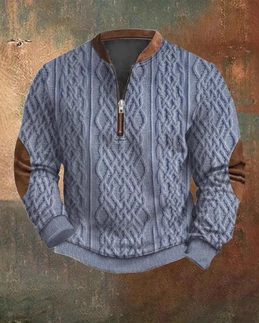 Grauer Strickpullover mit Zopfmuster, Reißverschluss und braunen Lederakzenten an Ellbogen und Kragen vor rustikalem Hintergrund.