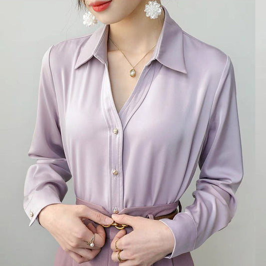 Frau in eleganter, lila Seidenbluse mit Knopfleiste und Blumenohrringen, trägt goldene Halskette. Mode, Damenbekleidung, Stilvoll.
