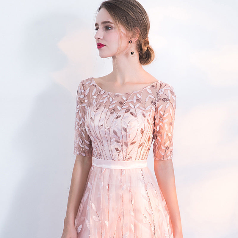 Frau in elegantem, rosa Abendkleid mit floralen Stickereien, halblangen Ärmeln und weißem Gürtel. Perfekt für formelle Anlässe und Hochzeiten.