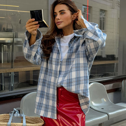Frau in kariertem Hemd und rotem Rock betrachtet sich in einem Spiegel. Mode, Streetstyle, Herbstlook, urbane Kulisse, trendige Kleidung.